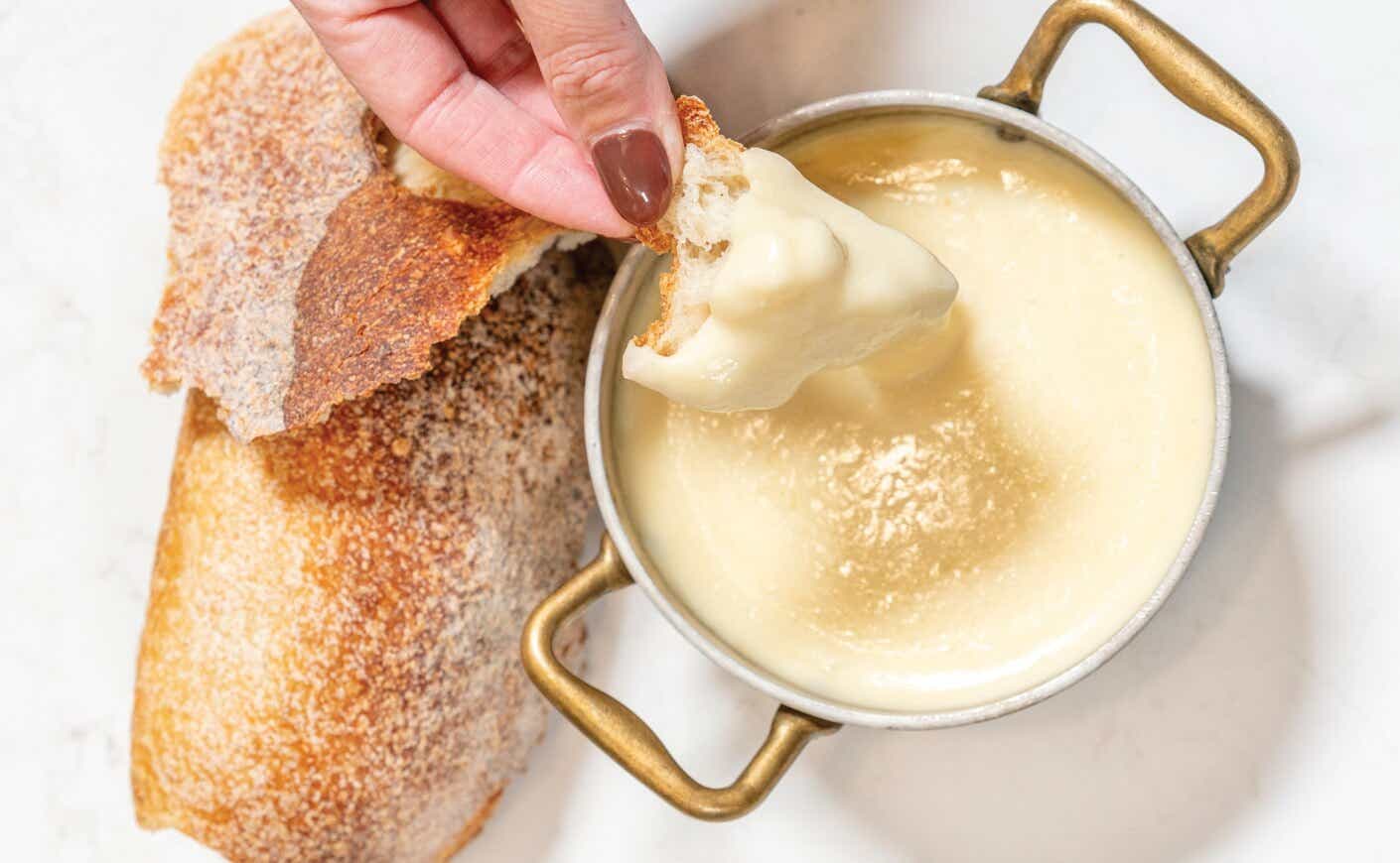 A hand dipping a piece of bread into a pot of fondue.