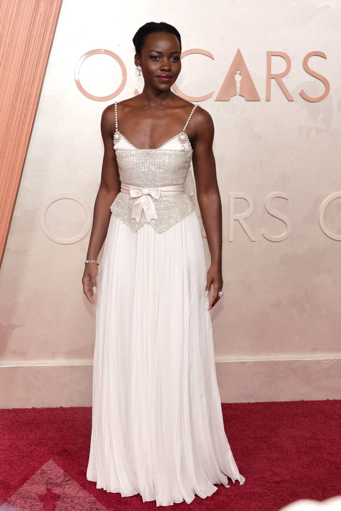 Lupita Nyong'o wears a light pink gown to the Oscars. The top bodice is very detailed with pearks and silver beading and a ribbon around the wiast.