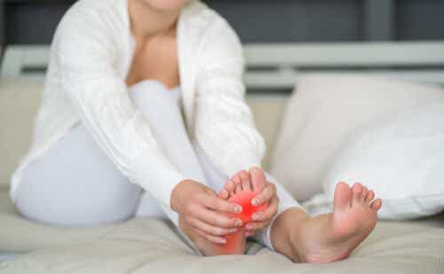 Woman holds the bottom of her foot, which is red with pain