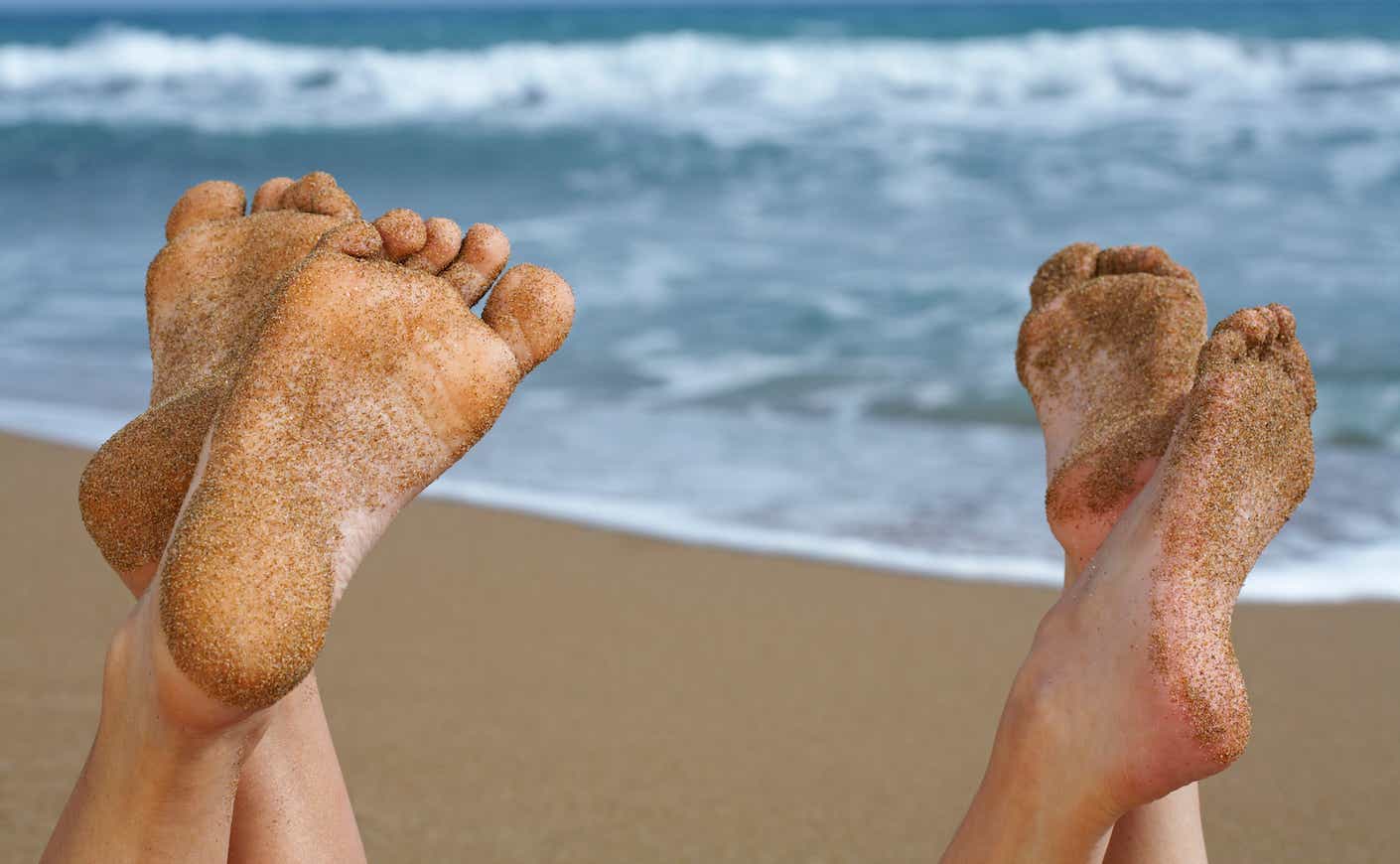 Two pairs of sandy feet on a beach