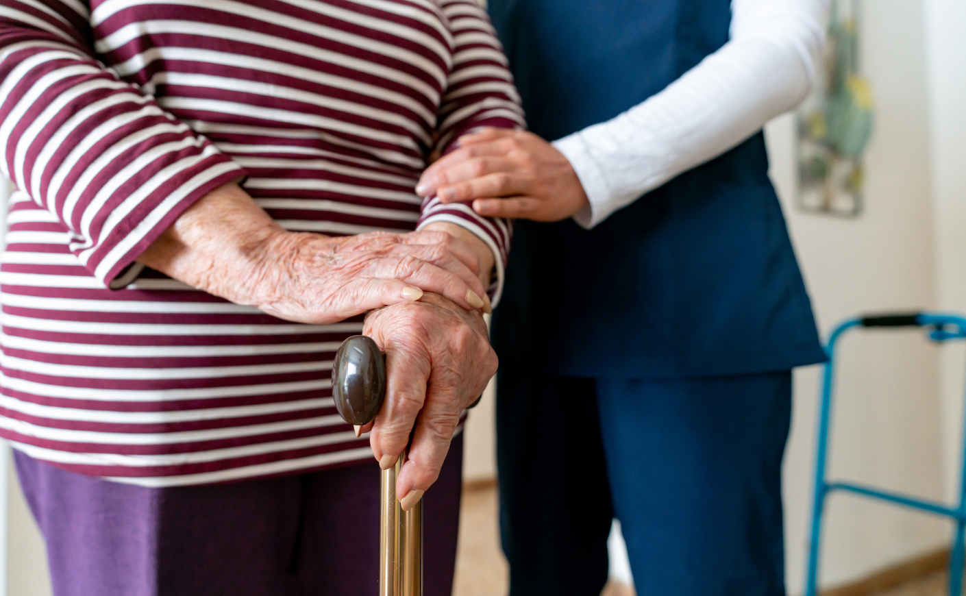 A nurse holding the arm of an elderly woman with a cane