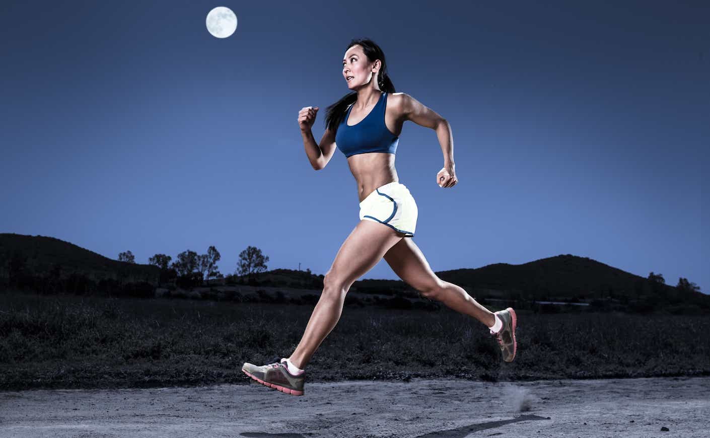 Female athlete runs under large full moon
