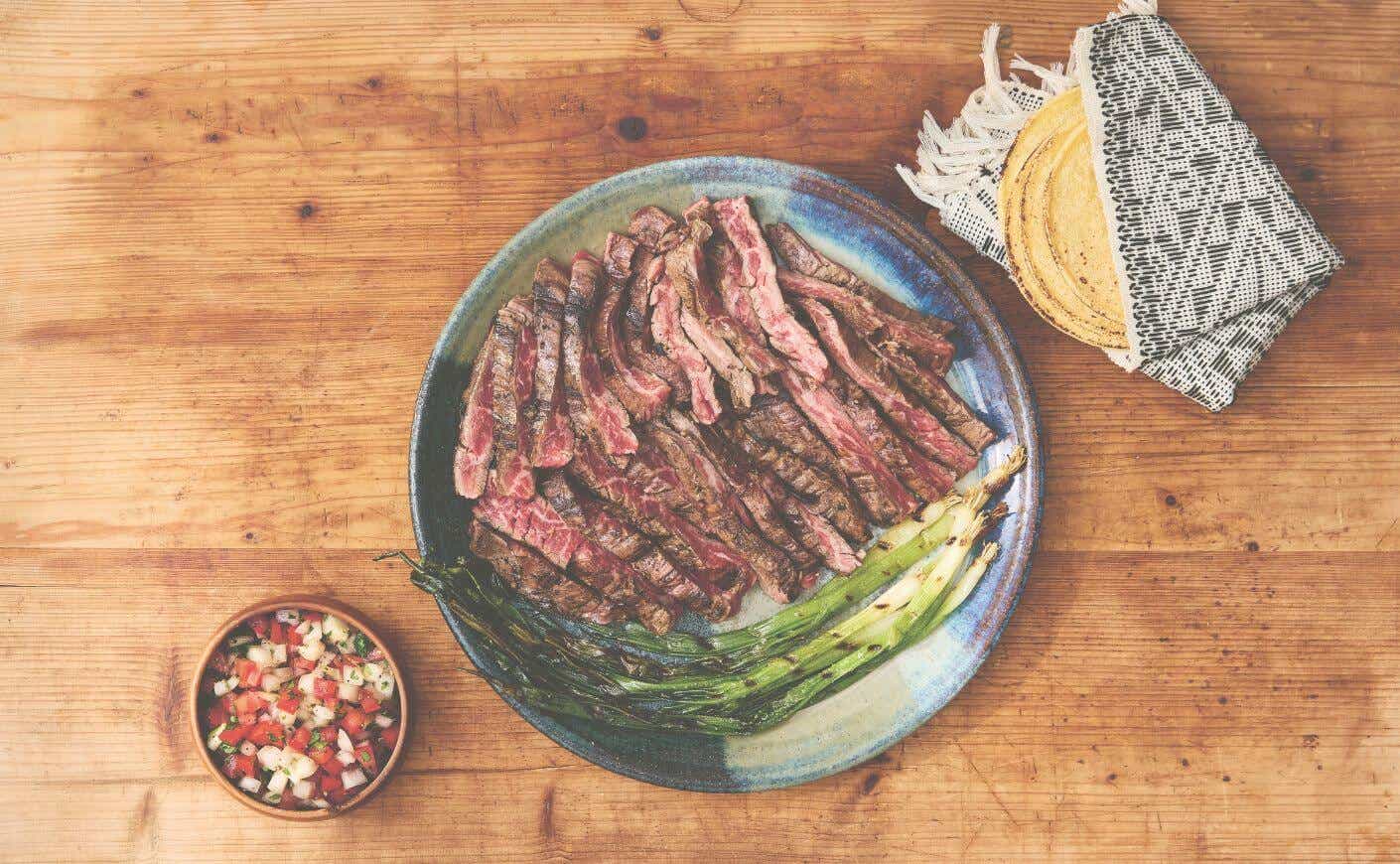 A dish of carne asada with pico de gallo and tortillas on the side.