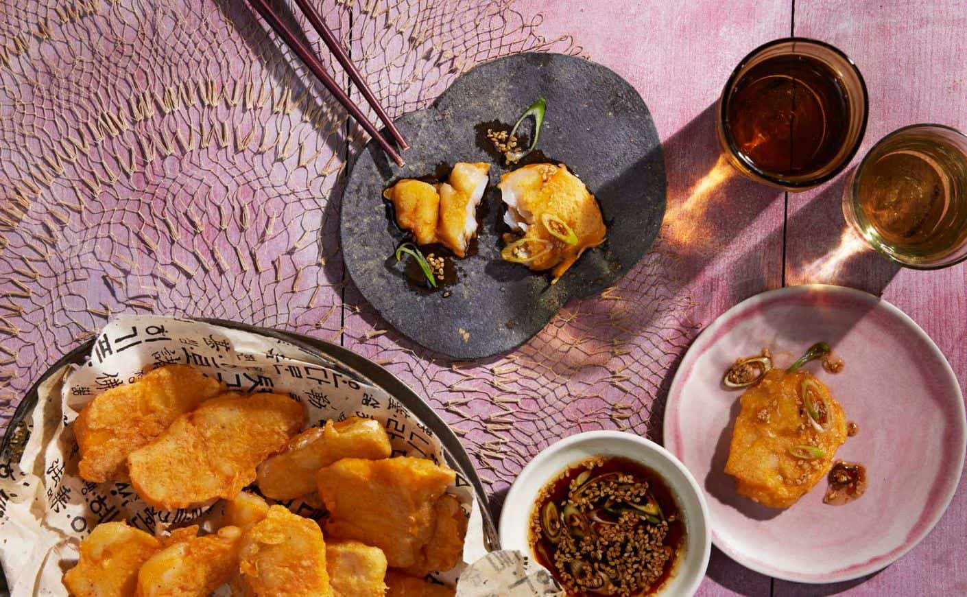 A plate of fried fish surrounded by dipping sauce and two beverages.