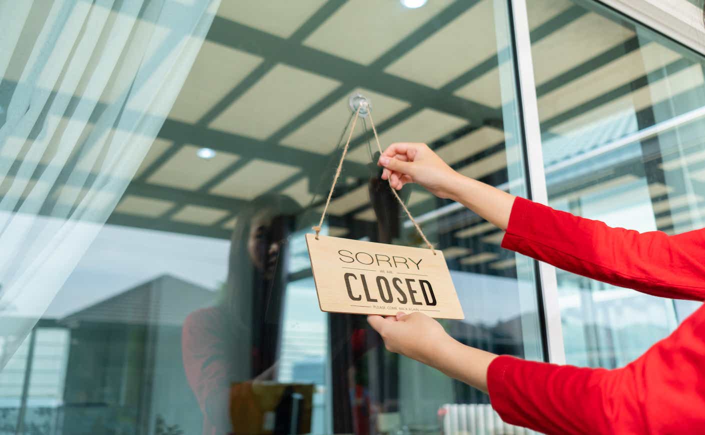 woman hanging a "sorry we're closed" sign on a storefront
