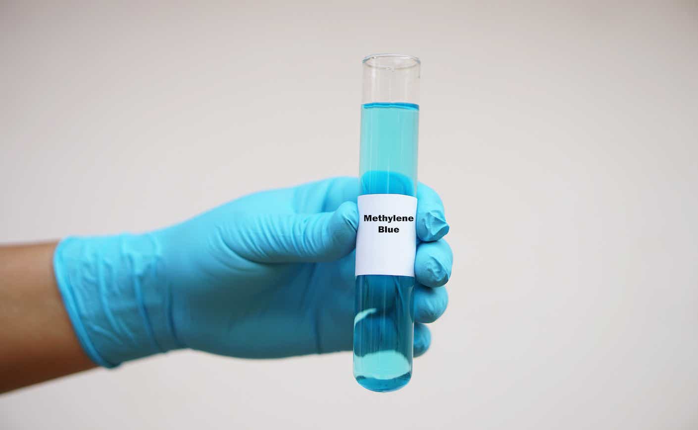 Close up chemist hand wears glove, hold test tube of Methylene Blue. Concept, Chemical used as a dye and as medication for methemoglobinemia treatment. Scientific experiment. Laboratory process.