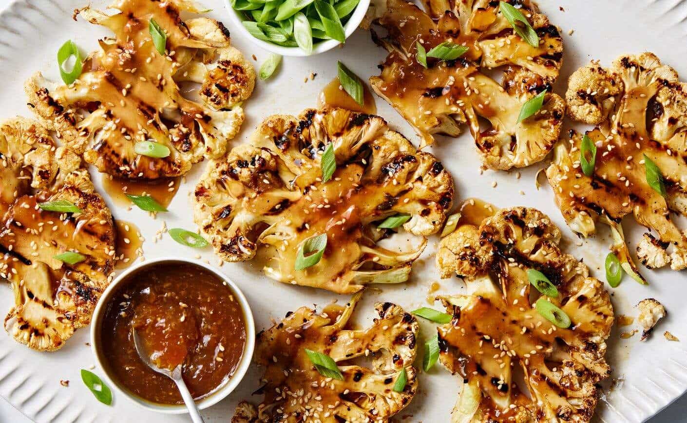 A plate of grilled cauliflower steaks covered with teriyaki sauce.