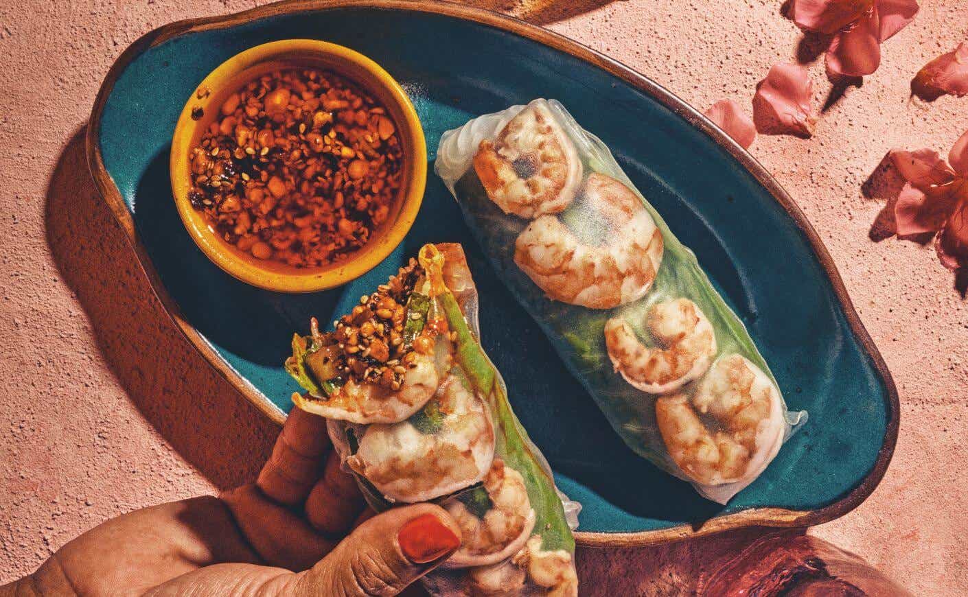 A hand dipping a spring roll into a ramekin of salsa macha.