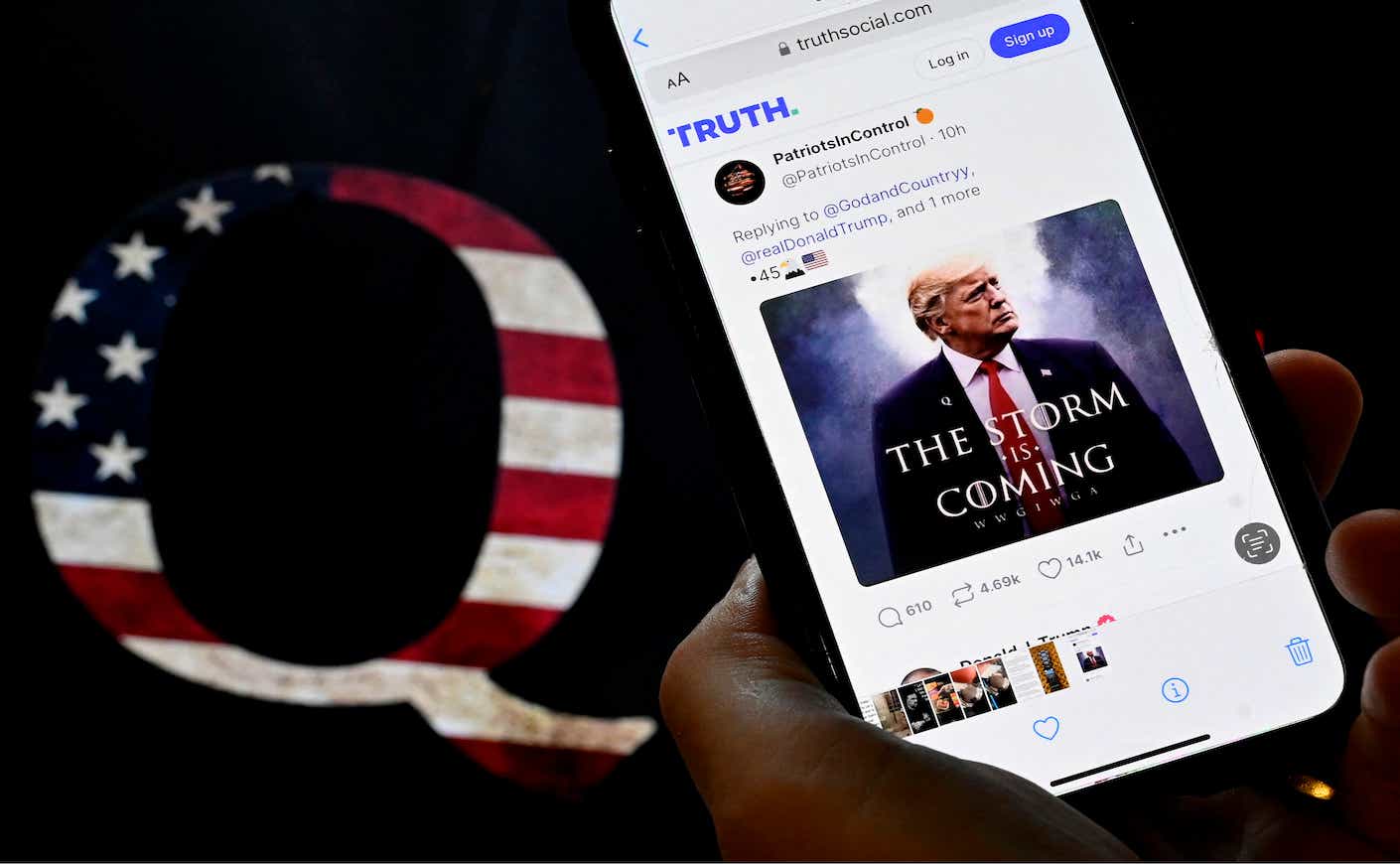 In this photo illustration, Donald Trump's TRUTH Social account is seen on a mobile device with an image of a QAnon sticker in the background in Washington, DC on September 13, 2022. (Photo by OLIVIER DOULIERY / AFP)