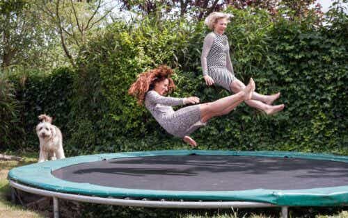 Two older women jumping on trampoline with a dog in the background