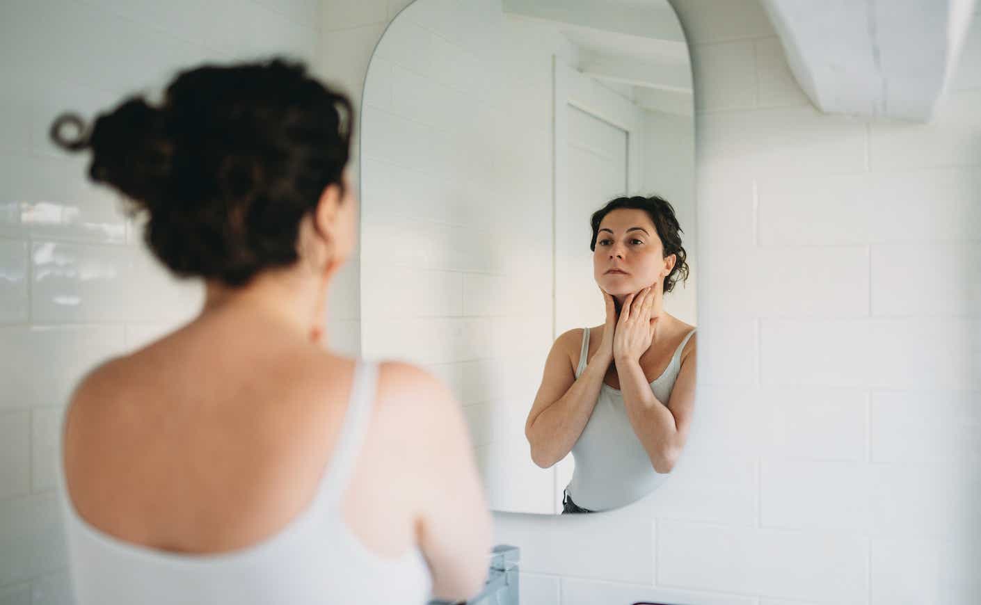 Woman looking in mirror with hands on her neck