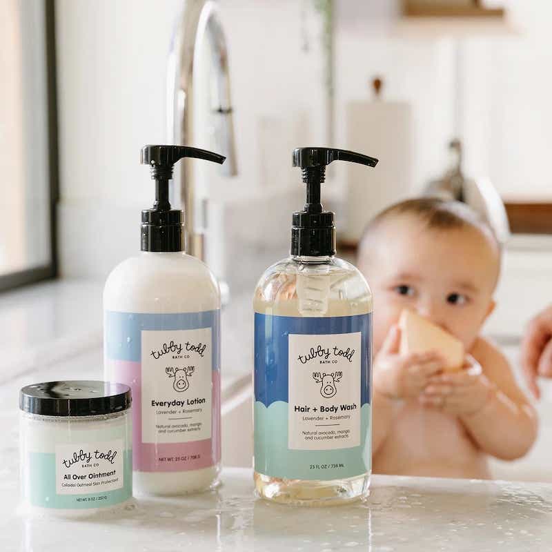 three bottles of Tubby Todd ointment, lotion, and body wash with a baby in the background