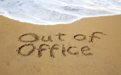 "Out of office" written in the sand at a beach