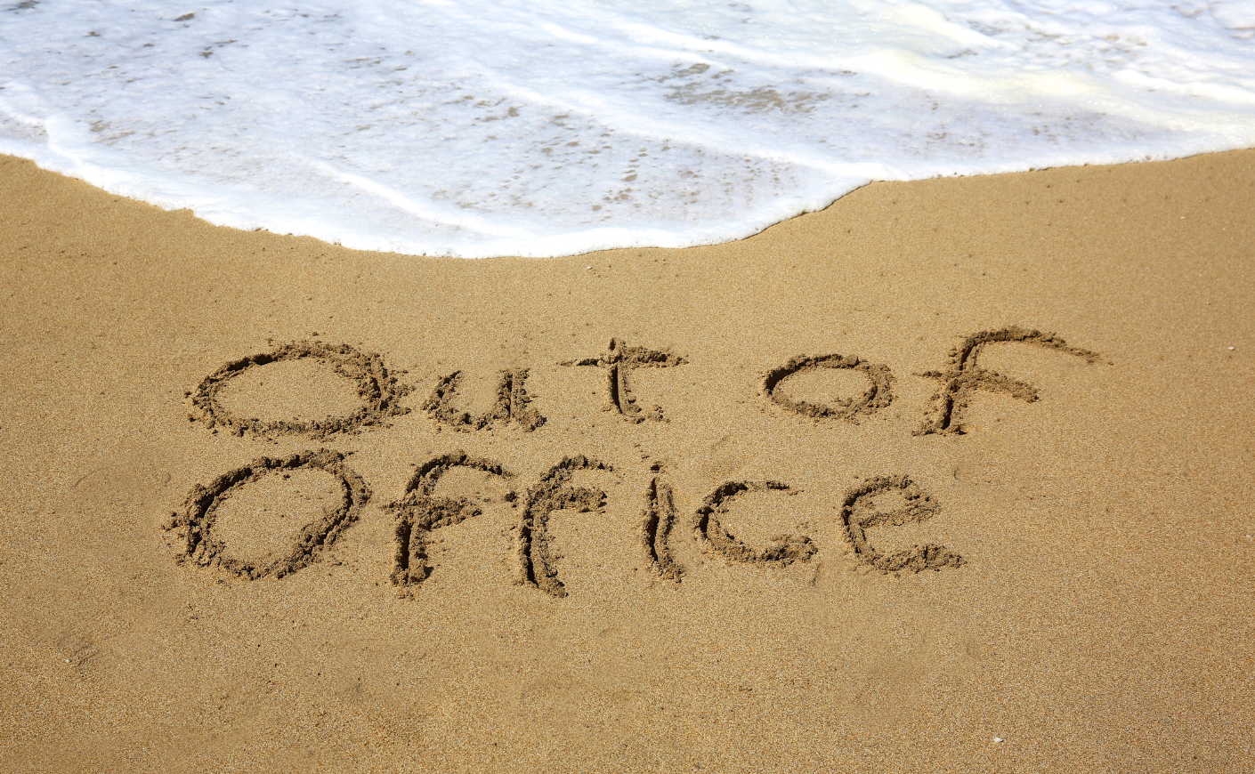 "Out of office" written in the sand at a beach