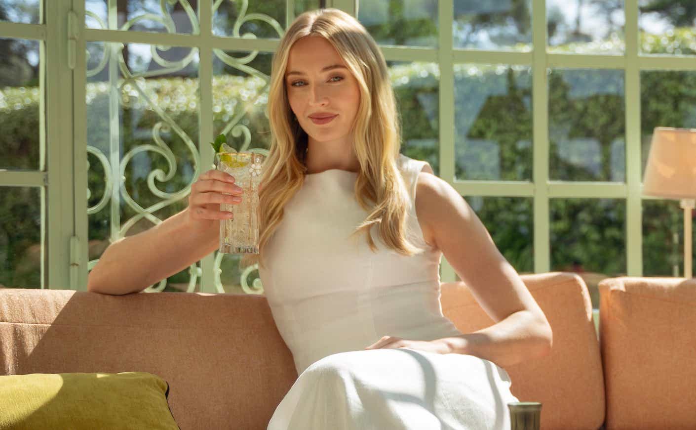 sophie turner sitting on a couch holding a Hugo Spritz cocktail