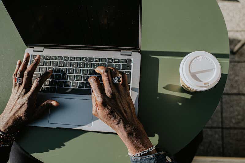 Corporate image of hands typing on a laptop keyboard in an outdoor environment, perhaps a balcony, a garden or a rooftop terrace.