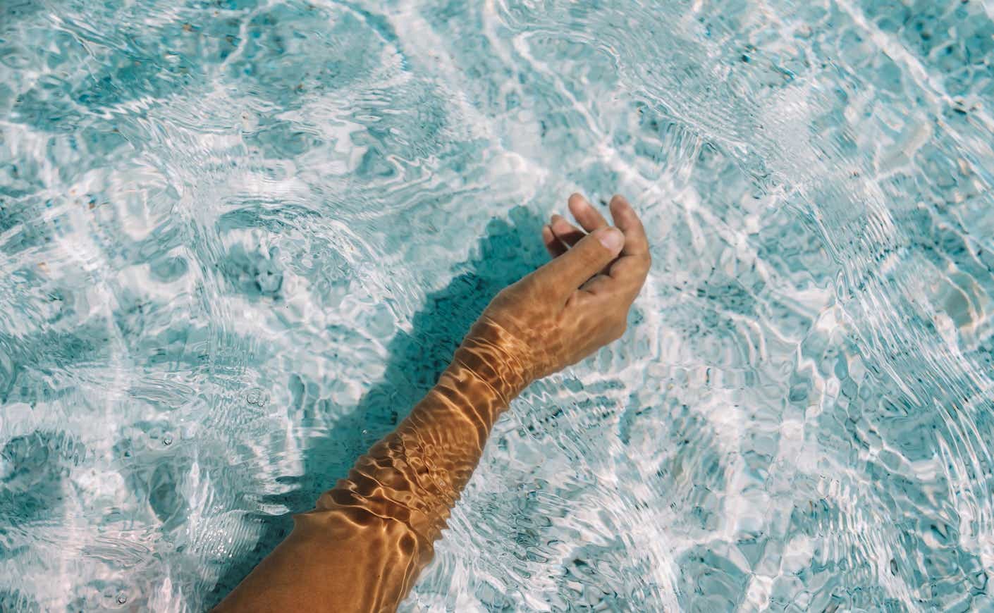 A woman's hand under clear water, beautiful sun glare on the skin.