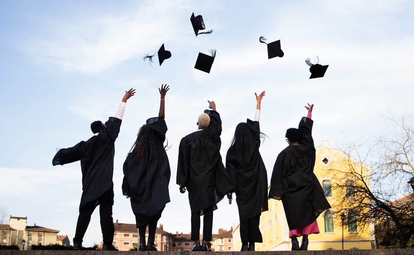Five recent graduates throw their caps in the air, backs facing the camera