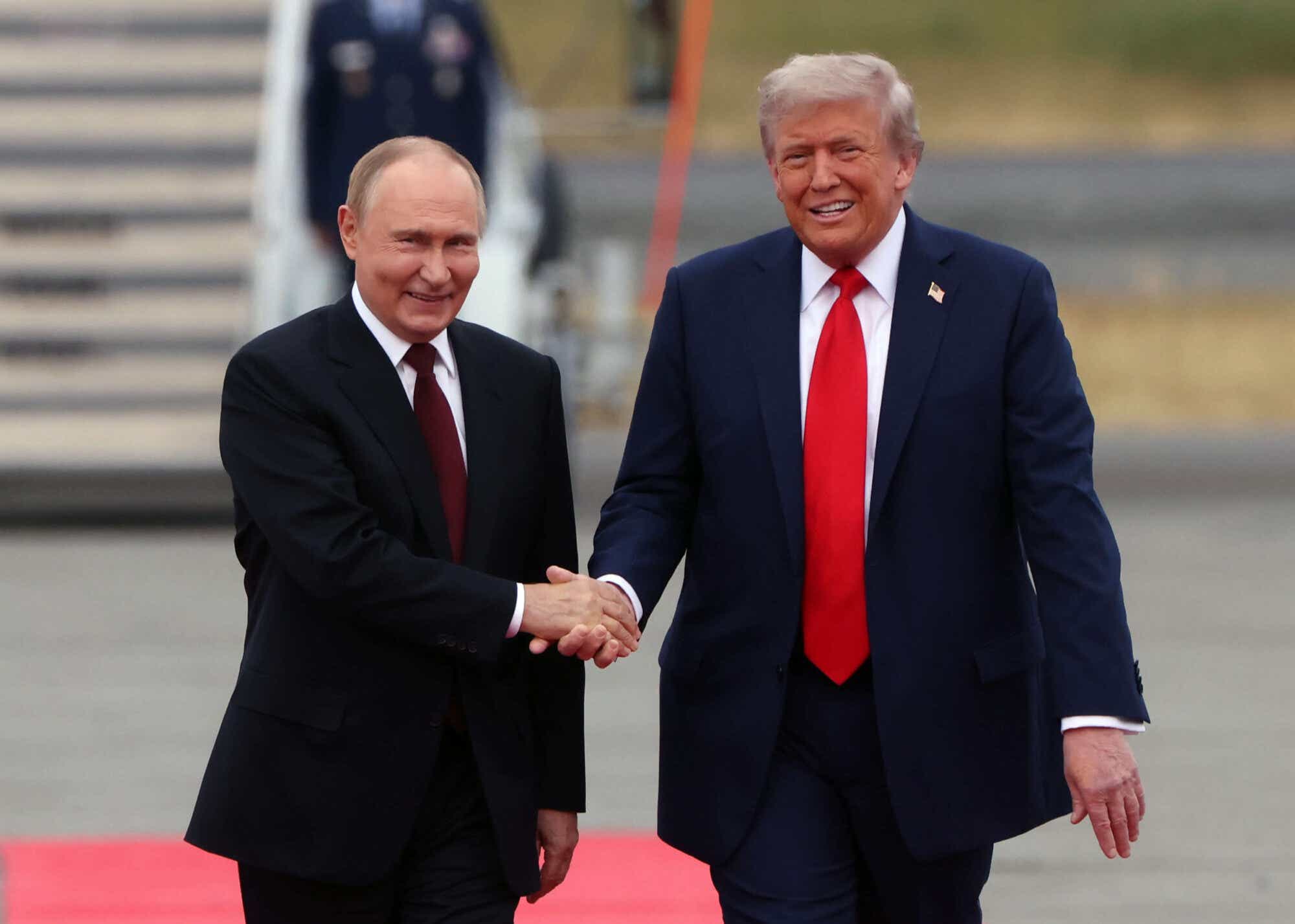 President Trump and Russian President Putin shaking hands outside Airforce One and smiling.