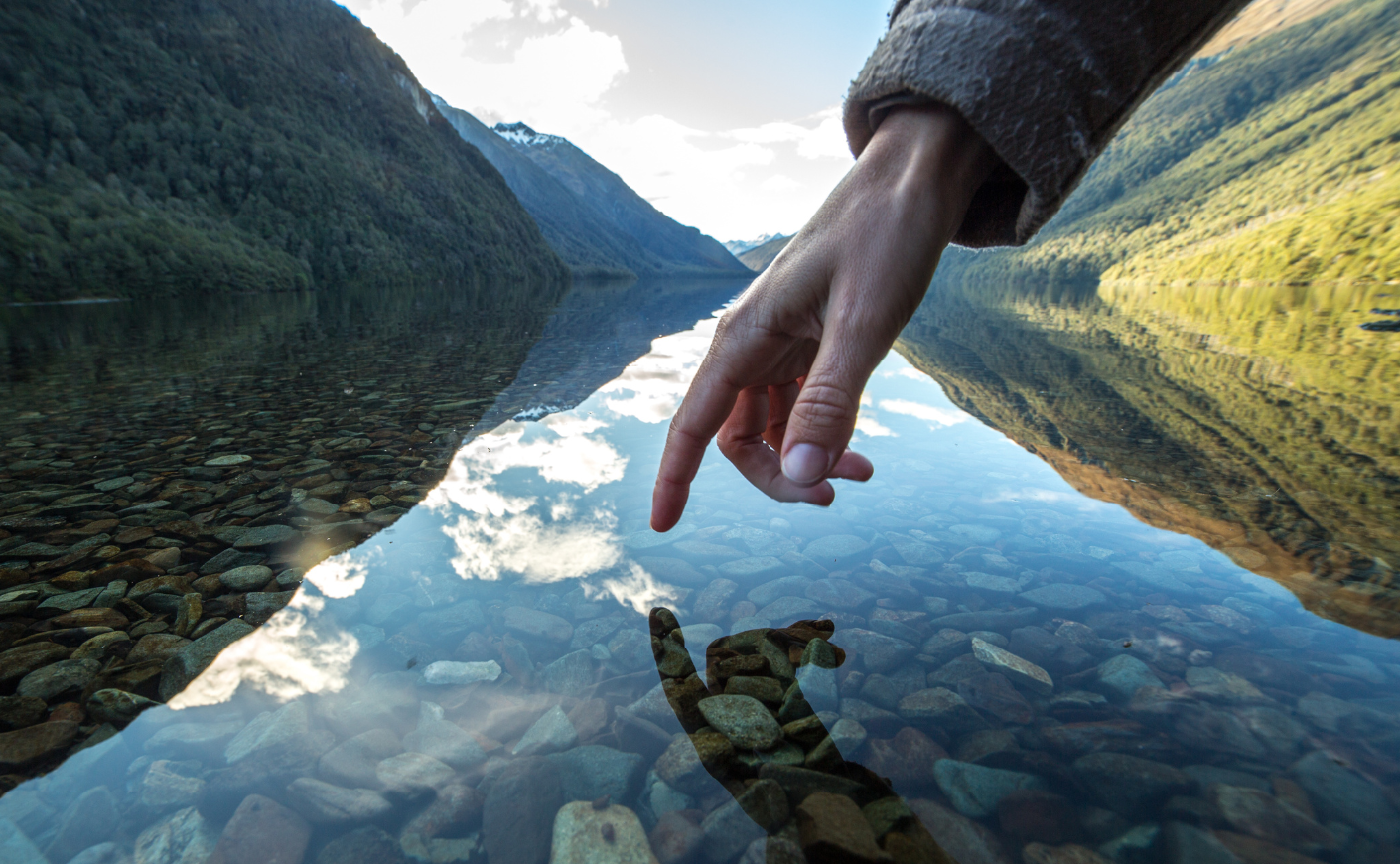 Hand touching crystal clear water next to a mountain