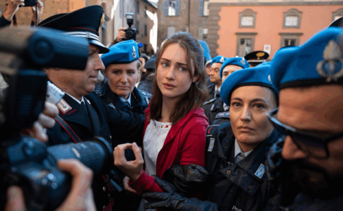 Grace Van Patten as Amanda Knox, surrounded by paparazzi and Italian carabinieri in blue hats