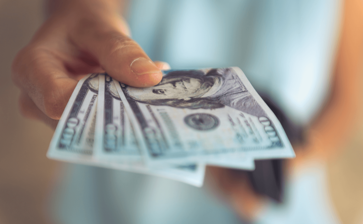 Close-up of hand holding out 3 100-dollar bills
