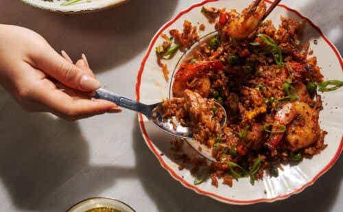 Two hands reaching utensils into a bowl of fried rice.