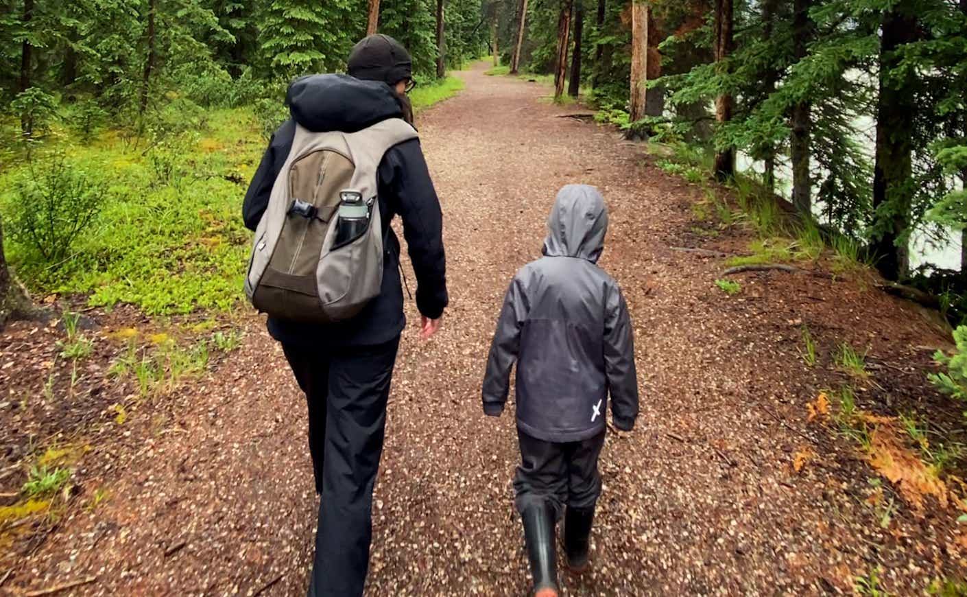 Man walks beside young boy in forest, both wearing rain coats