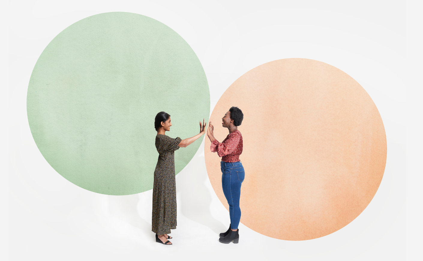Two women standing in their own respective circles but meeting hands in the middle
