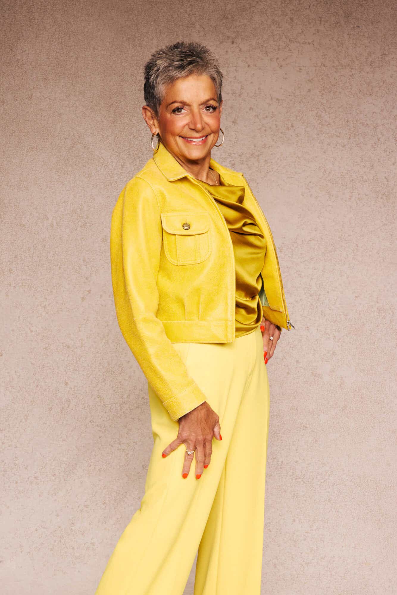 Diane sports a yellow leather jacket, a mustard-colored draped top, and butter-yellow pants