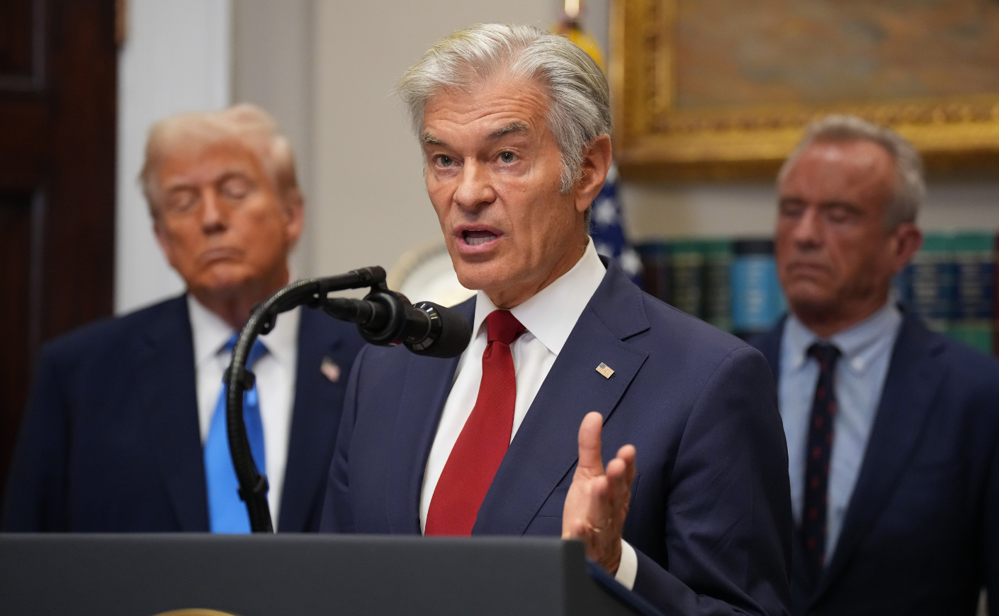 Dr. Oz stands at a pulpit in front of President Trump and HHS Secretary RFK JR.