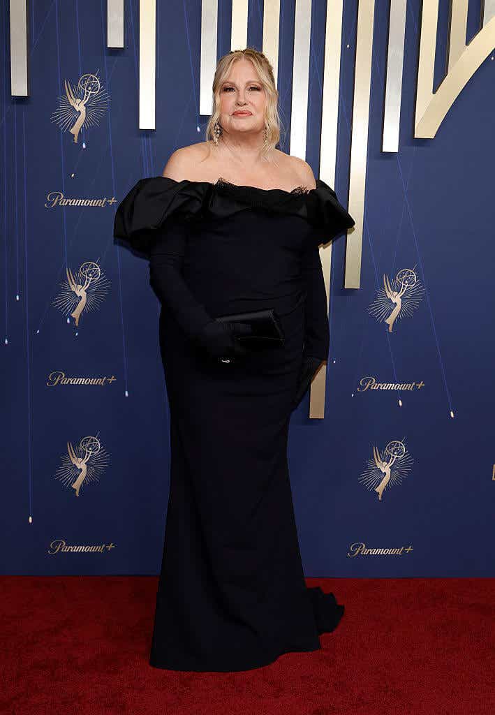 Jennifer Coolidge wears an off-the-shoulder black down with a ruffled neckline and black gloves