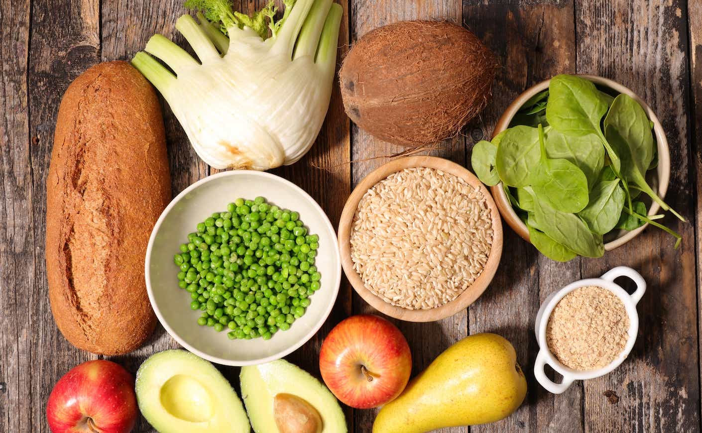 A pile of fiber-rich foods, including loaf of bread, avocados, and apples