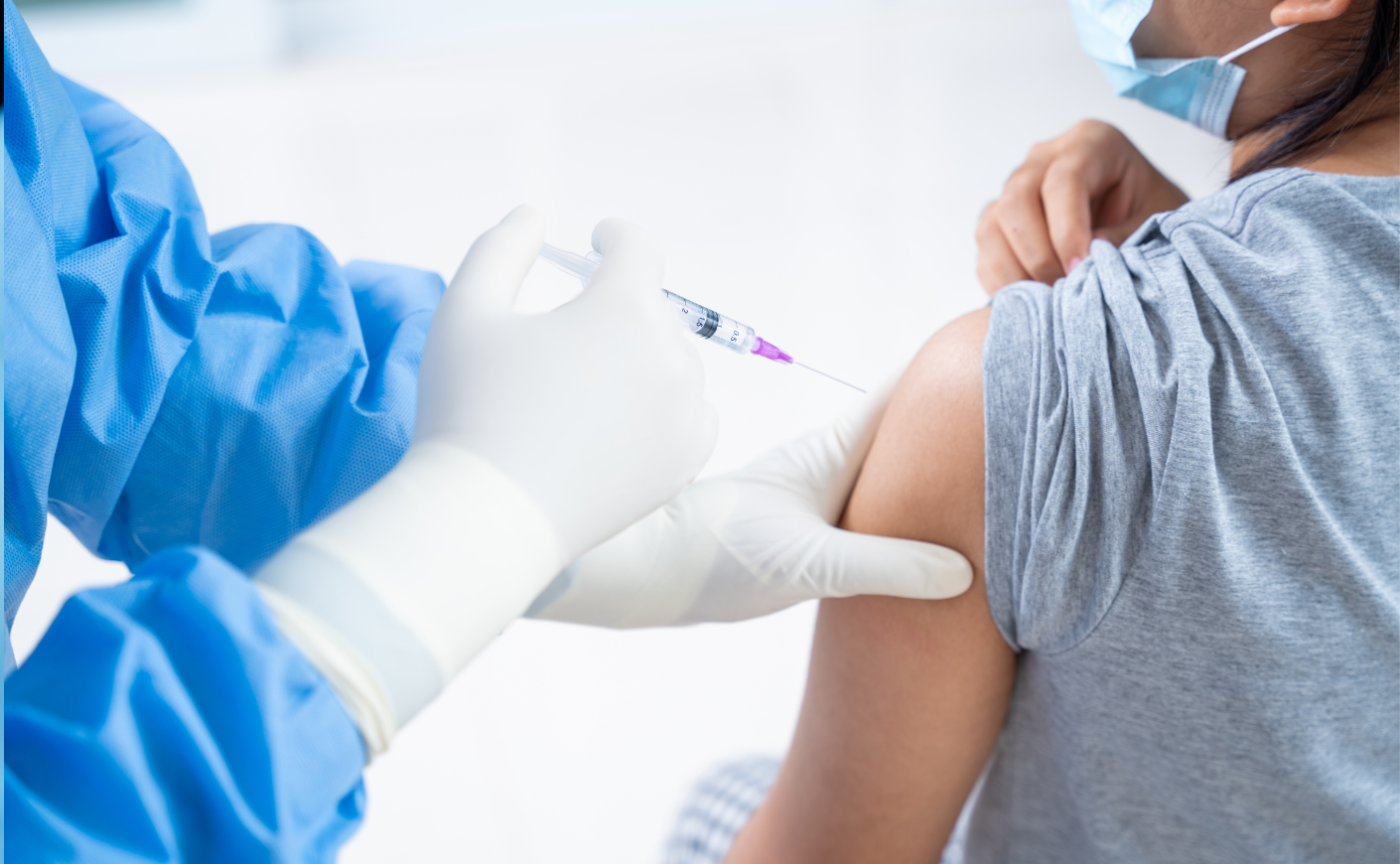 A medical professional in scrubs giving a vaccine to a person in a surgical mask