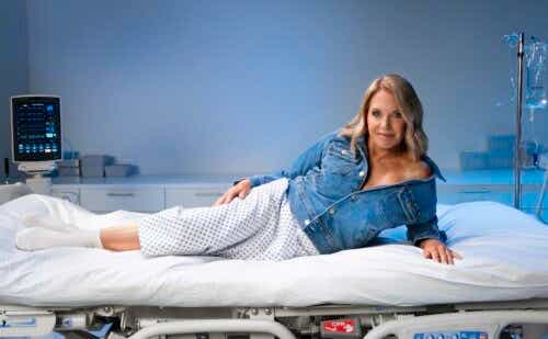 katie couric laying on an exam table in full glam with a denim jacket on over her hospital gown