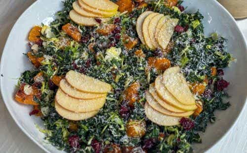 A bowl of kale, squash, and apple salad in walnut dressing and covered in parmesan cheese.