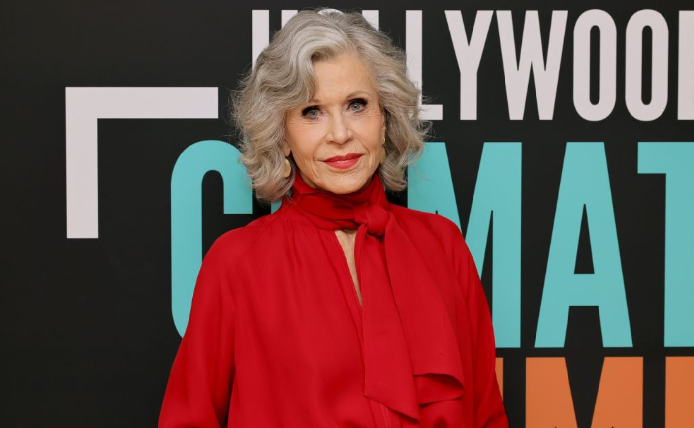 Jane Fonda wears a red blouse with a matching scarf and a bold red lip.