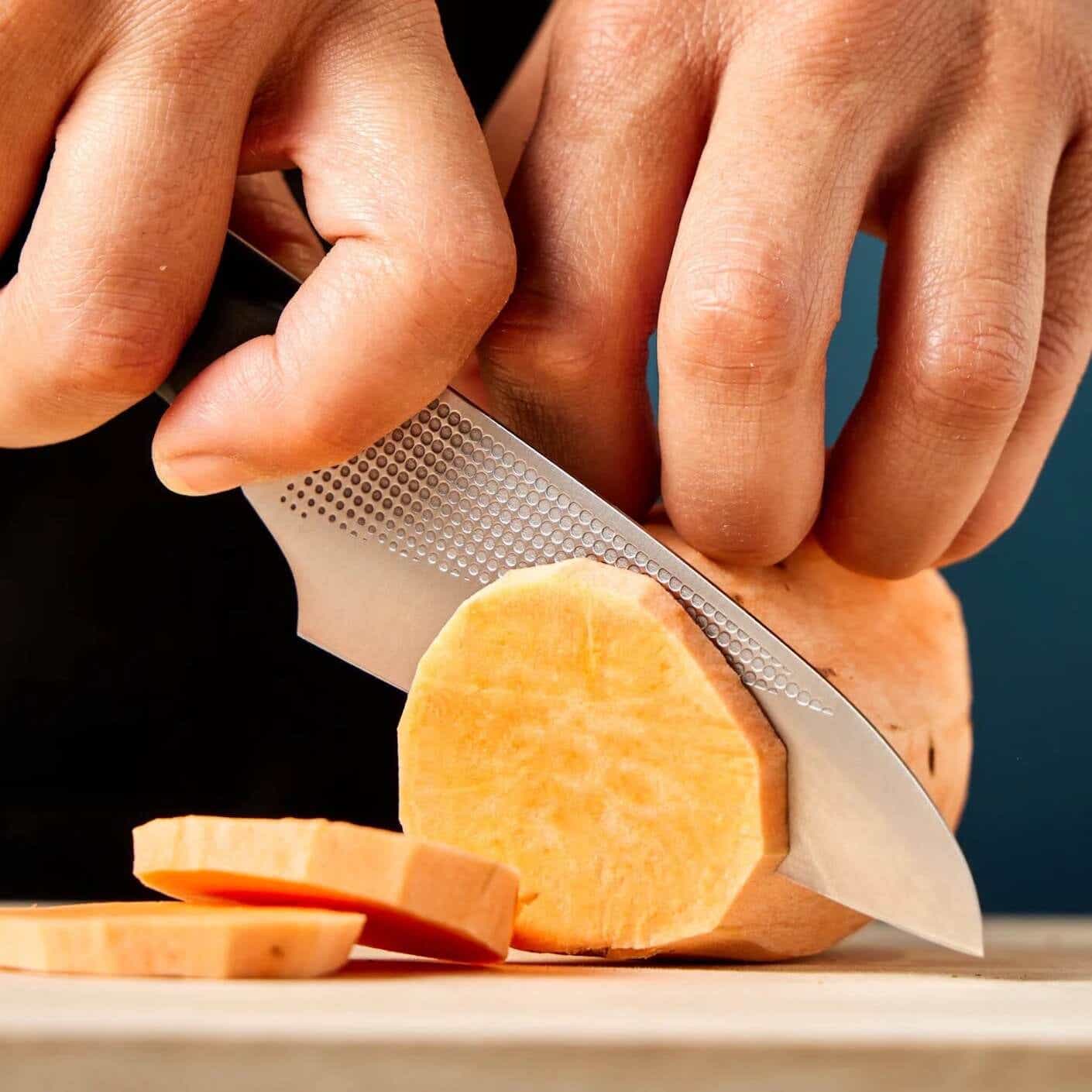 A hand using a kitchen-kiji knife to slice a sweet potato.