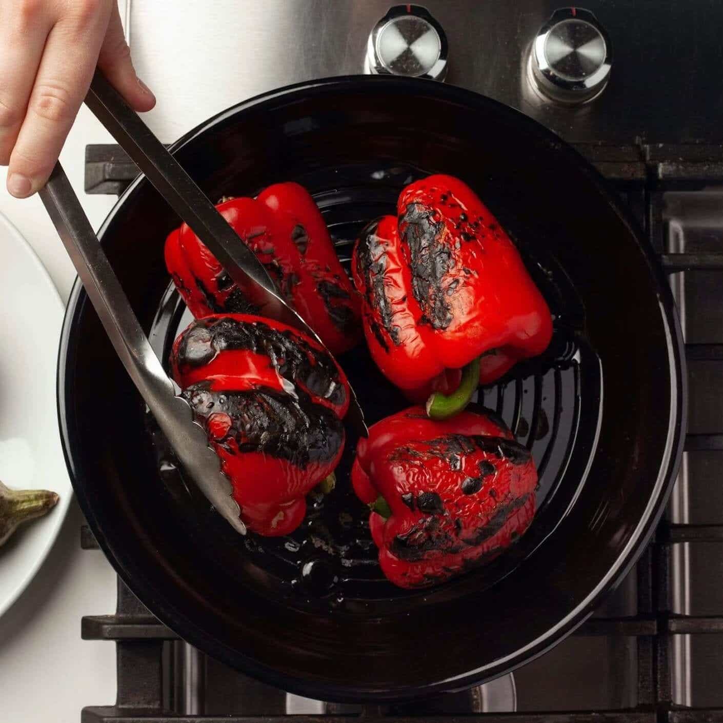 Three red peppers charring on a Közmatik.