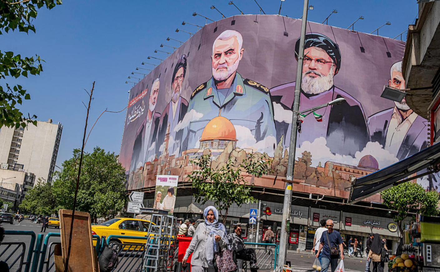 Iranians walk past a billboard of the slain leaders of anti-Israeli groups, including former Hamas political chief Yahya Sinwar.
