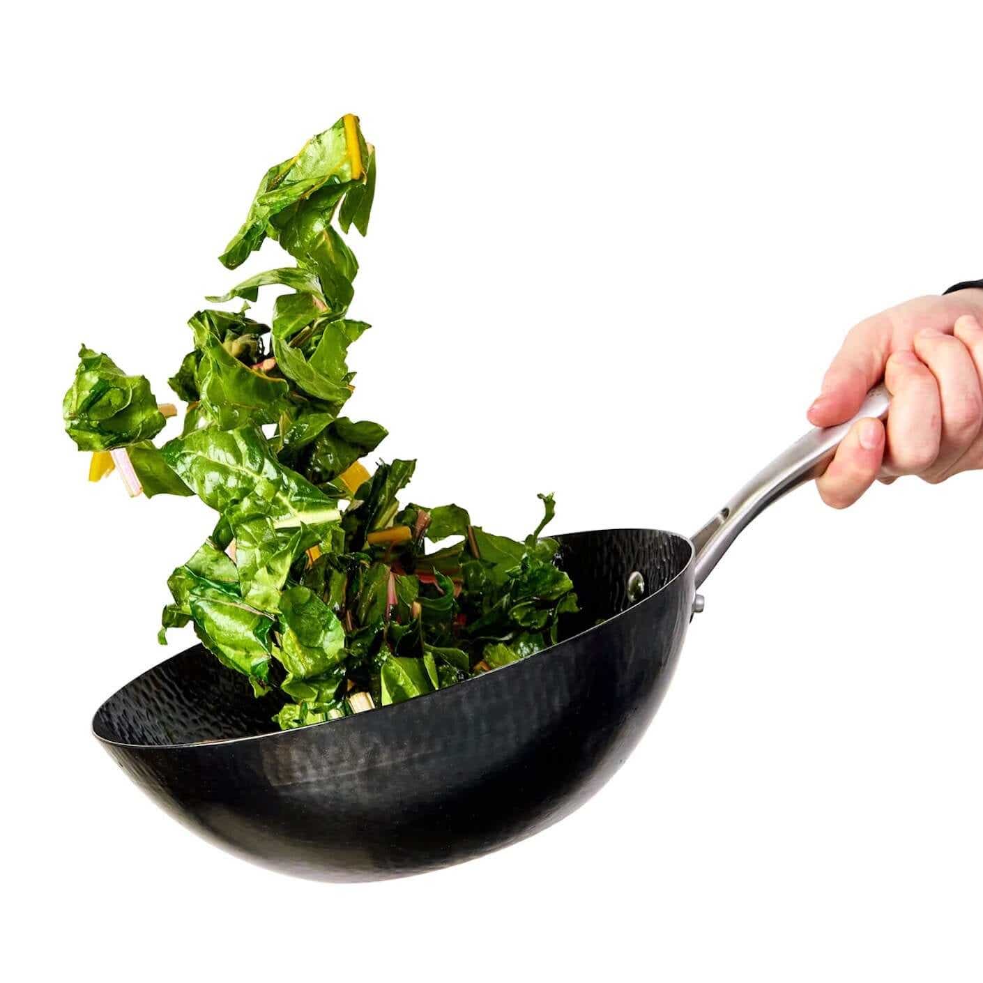Greens being tossed in a small wok.