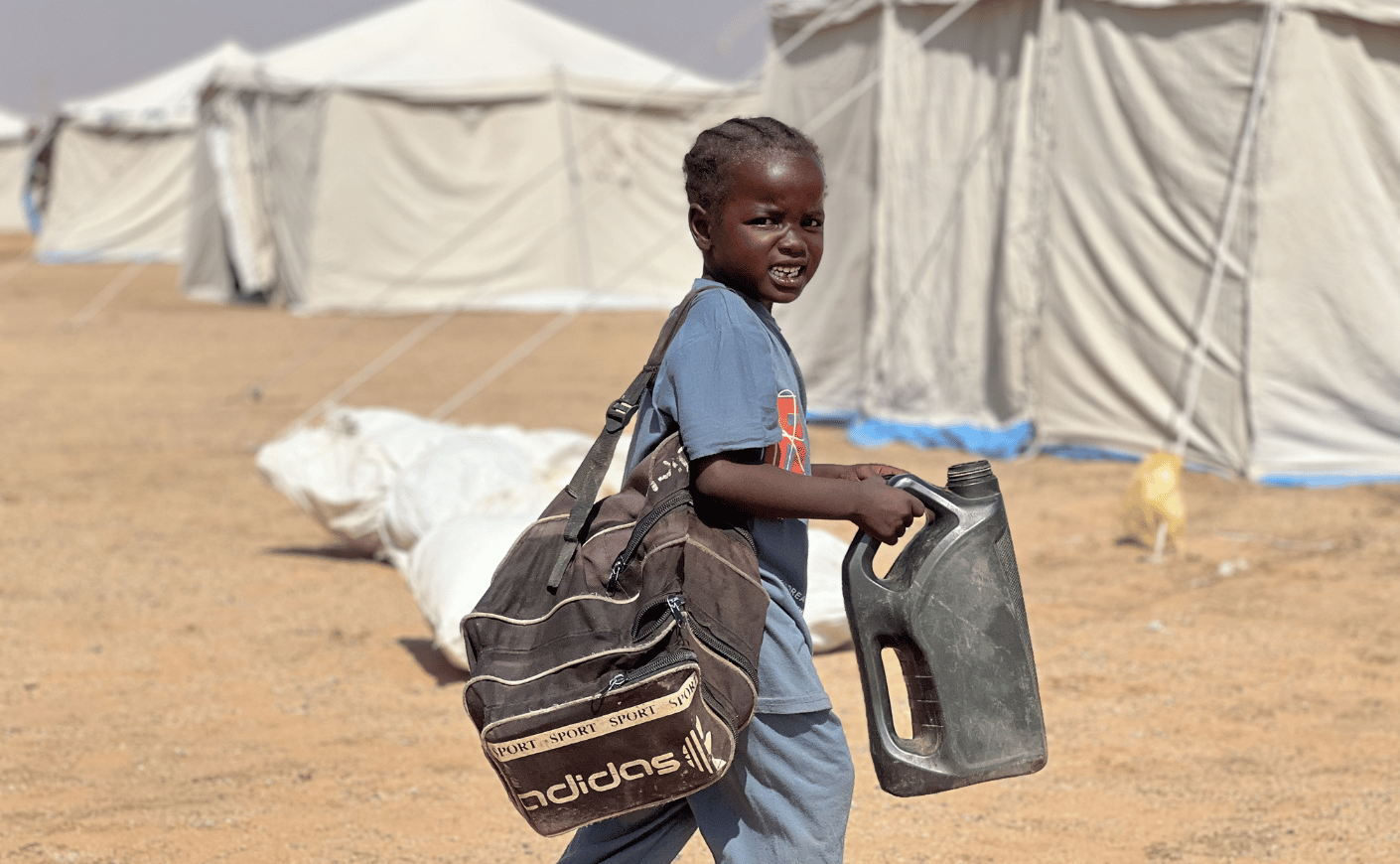 A child carries a water jug in the newly established El-Afadh camp in Al Dabbah, in Sudan's Northern State