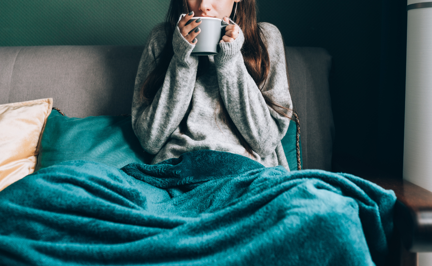 Woman sipping from a mug with a teal blanket draped over her legs