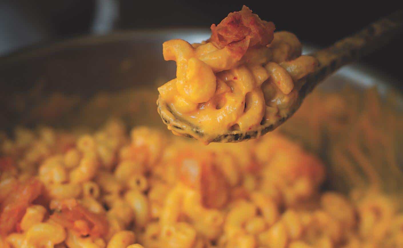 A wooden spoon scooping creamy vegan kimchi mac and cheese.