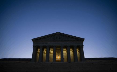 The Supreme Court stands dark except for one light in the middle, against a dark blue sky