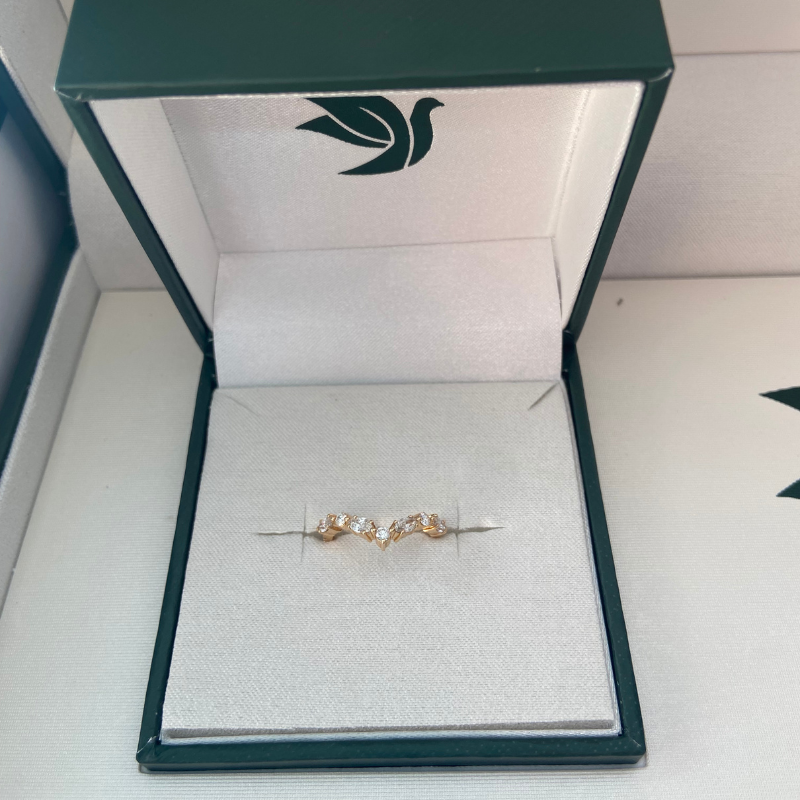 A gold and diamond wedding band in a green box