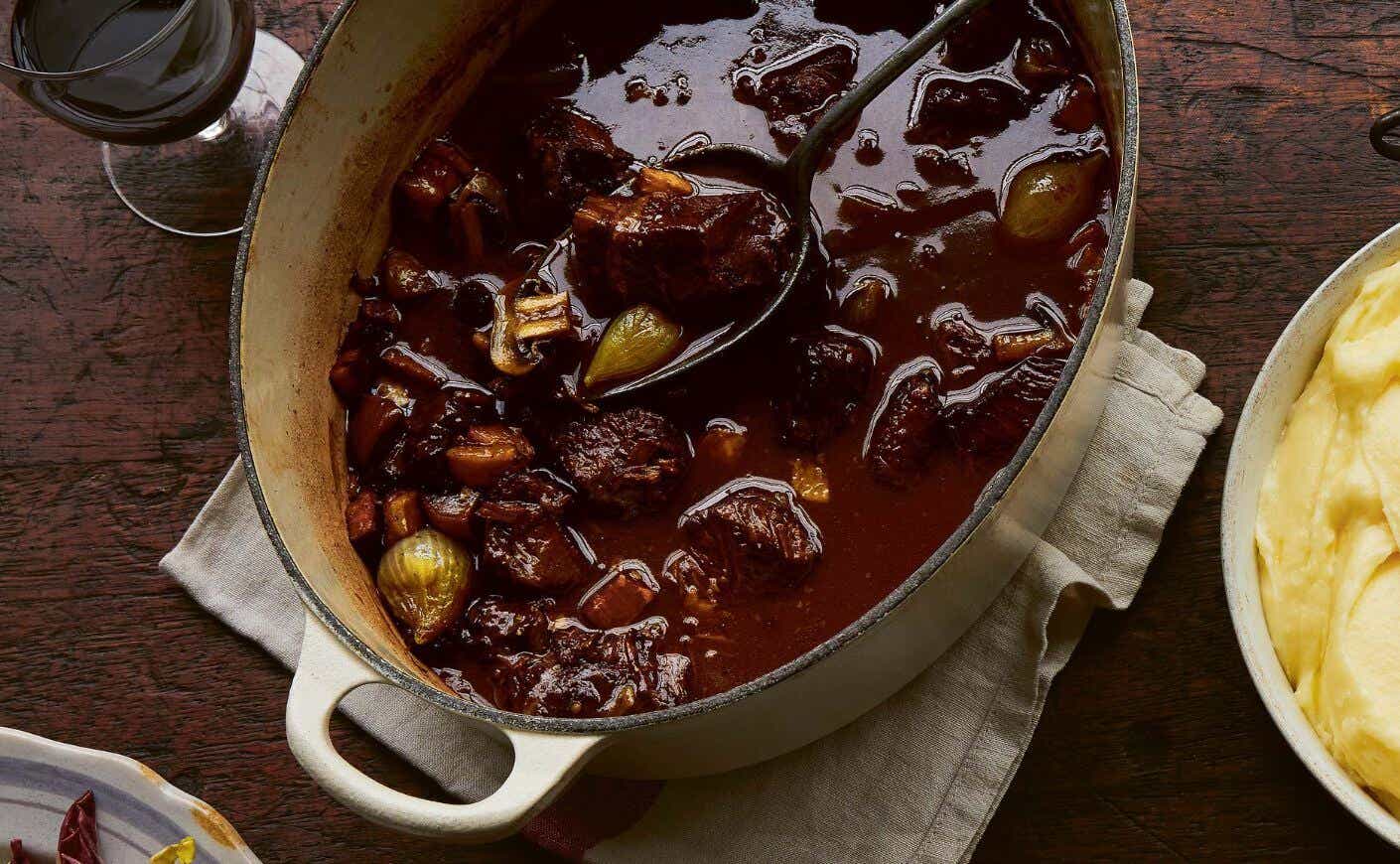 A Dutch oven of beef bourguignon on a table next to a dish of mashed potatoes.