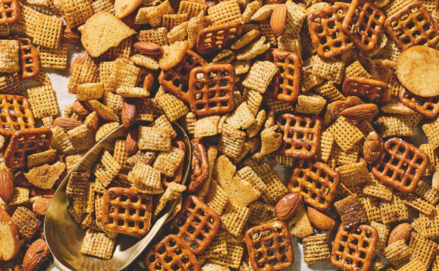 A spoon scooping from a tray of Chex mix.
