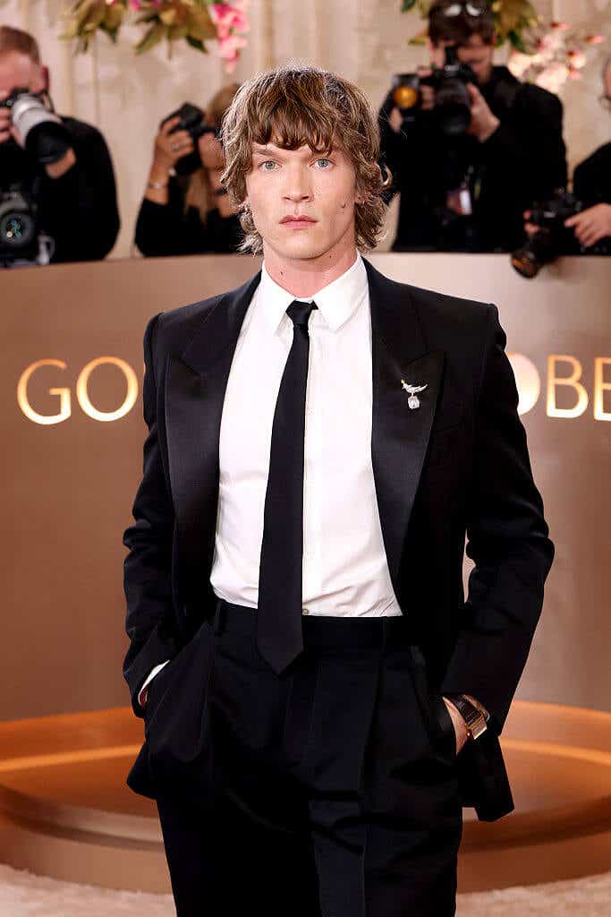 Connor Storrie wears a black tux with a silver diamond pin to the Golden Globes
