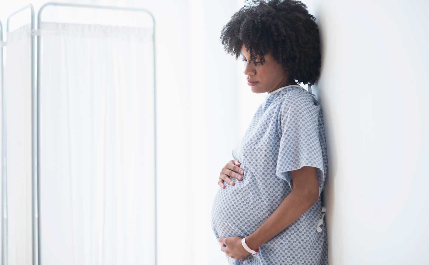 black woman in a hospital gown holding her pregnant belly